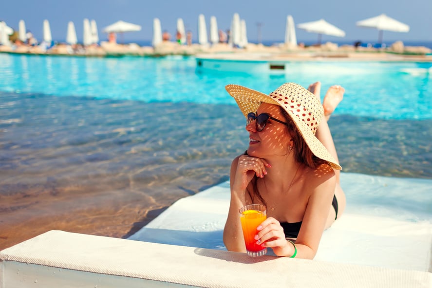 Woman relaxing in hotel swimming pool lying on chaise-longue with cocktail. Summer vacation. All inclusive